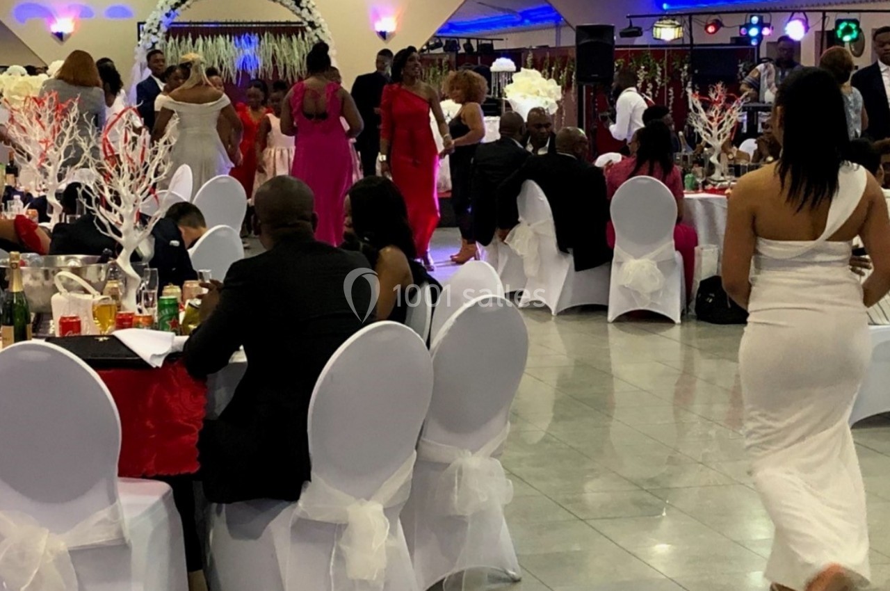 Salle de réception animée avec des invités assis à des tables décorées et d'autres dansant en arrière-plan.