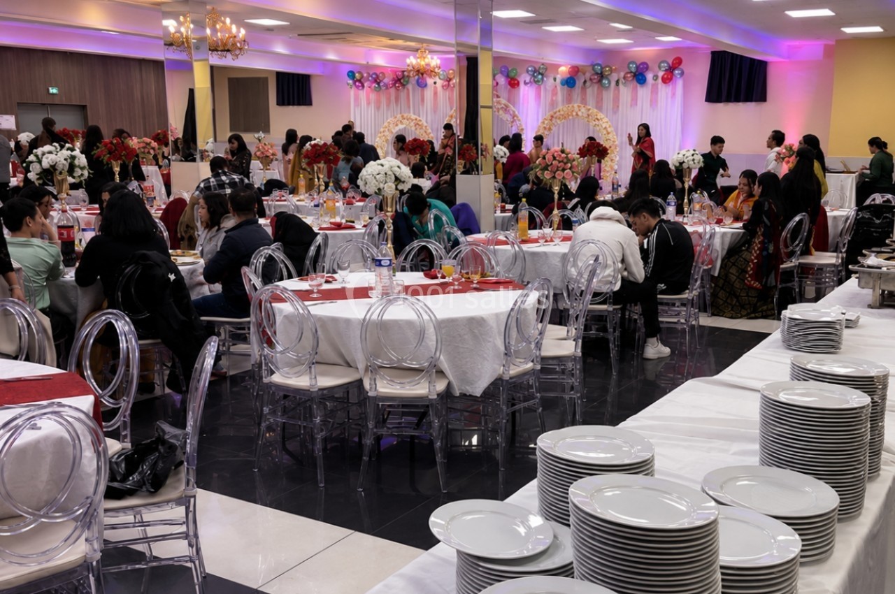 Salle de réception décorée pour un événement, avec invités assis et debout, tables dressées et buffet en arrière-plan.