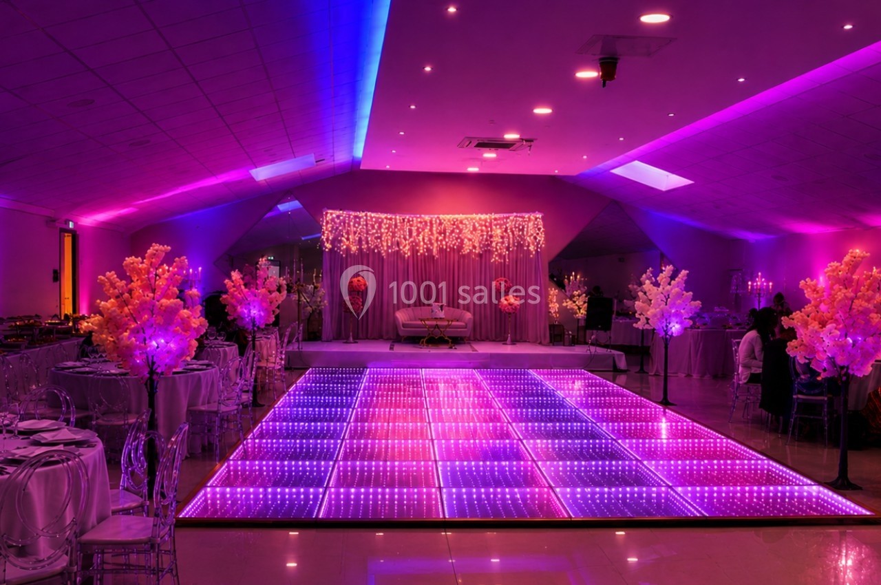 Salle de réception décorée avec un éclairage violet, piste de danse lumineuse et tables élégamment dressées.