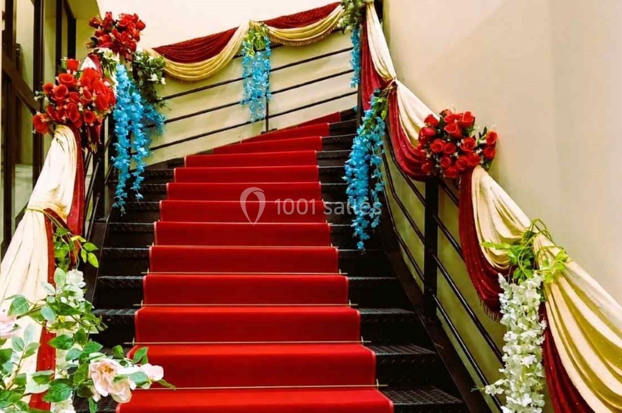 Escalier décoré de fleurs rouges, bleues et blanches, avec un tapis rouge et des drapés dorés et blancs.