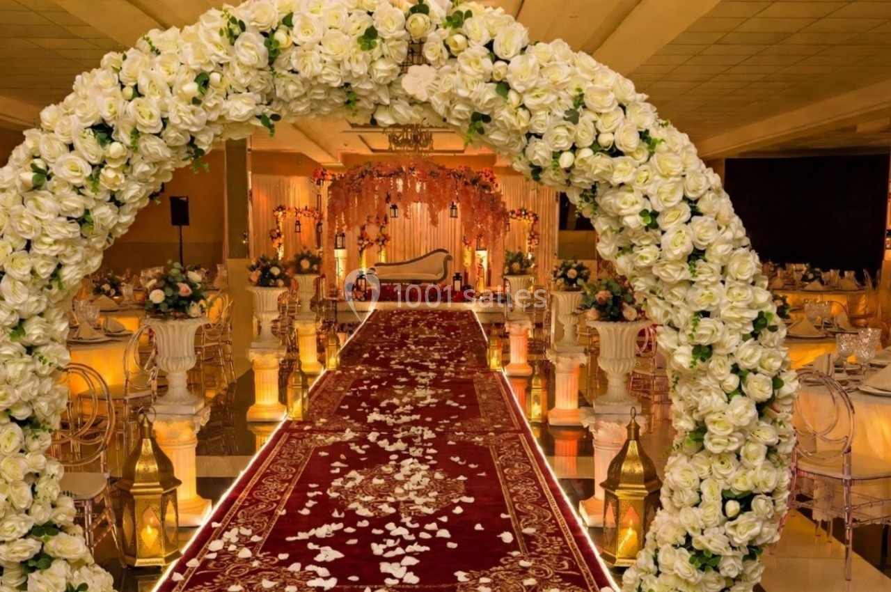 Arche de fleurs blanches encadrant une allée rouge décorée de pétales, menant à une scène ornée pour un événement.
