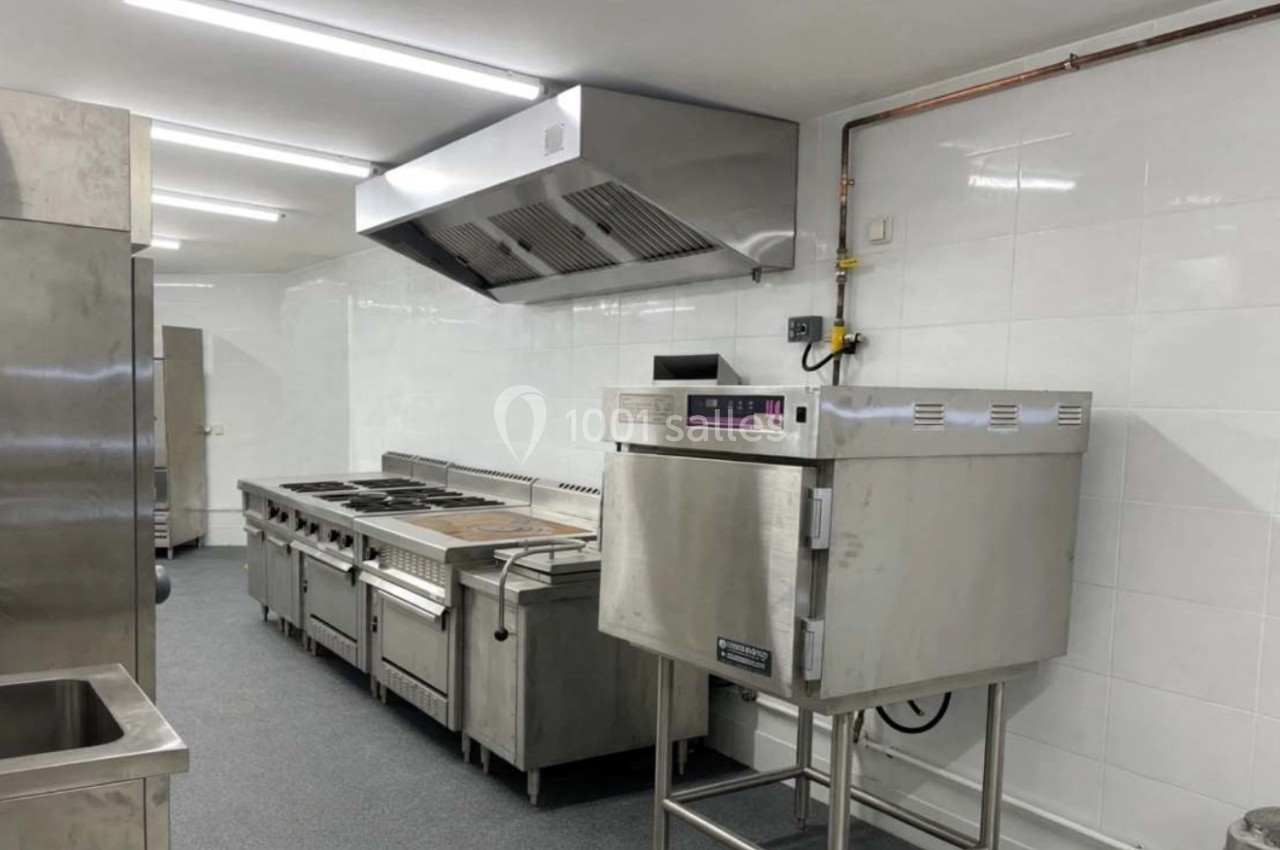 Cuisine professionnelle équipée avec four, plaques de cuisson, hotte et surfaces en acier inoxydable.