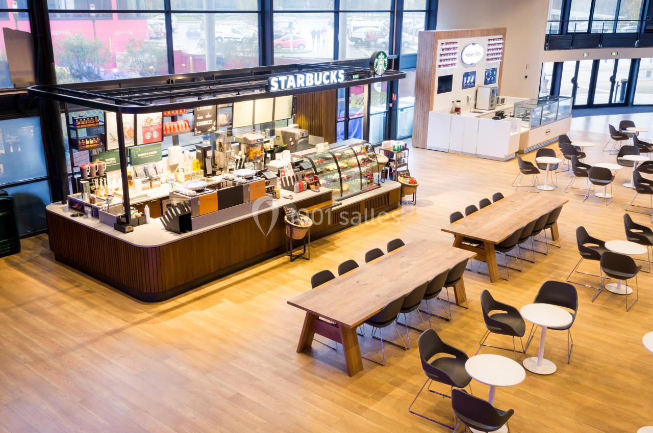 Comptoir Starbucks dans un espace lumineux avec tables, chaises et grandes baies vitrées en arrière-plan.