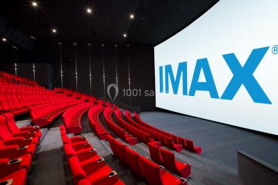 Salle de cinéma avec sièges rouges vides et grand écran affichant le logo IMAX.