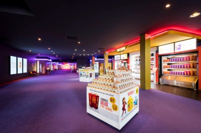 Salle de cinéma vide avec des rangées de sièges rouges et un projecteur allumé au fond.