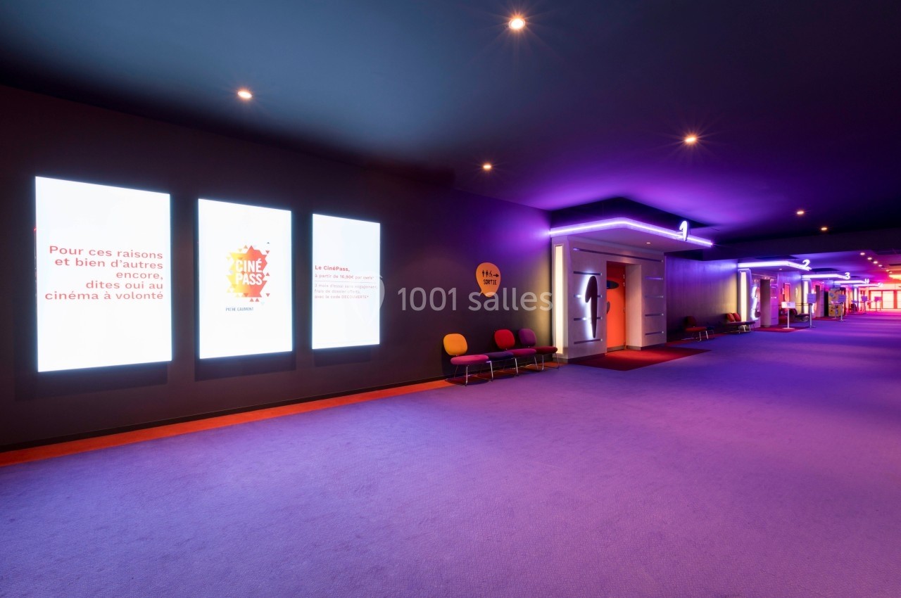 Couloir d'un cinéma avec affiches lumineuses, sièges colorés et éclairage violet.