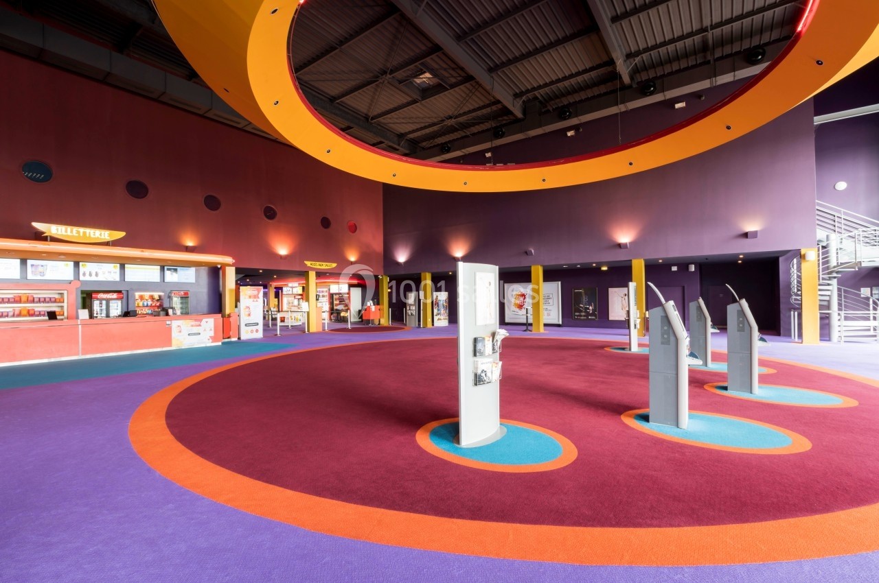 Hall d'entrée spacieux avec guichets, bornes interactives et éclairage coloré sous un plafond industriel.