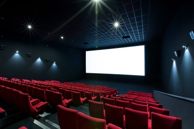 Salle de cinéma vide avec des rangées de sièges rouges et un projecteur allumé au fond.