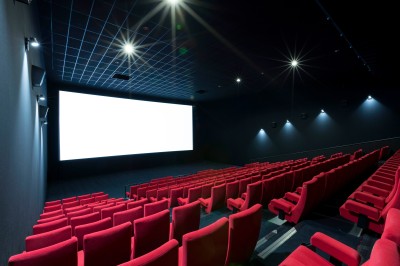 Salle de cinéma vide avec des rangées de sièges rouges et un projecteur allumé au fond.