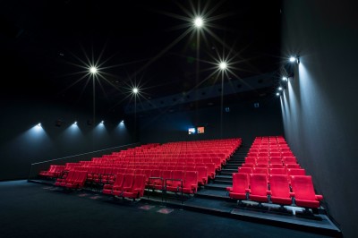 Salle de cinéma vide avec des rangées de sièges rouges et un projecteur allumé au fond.