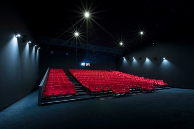 Salle de cinéma vide avec des rangées de sièges rouges et un projecteur allumé au fond.