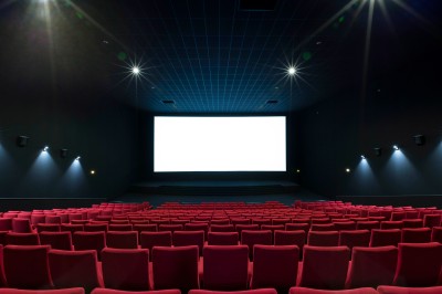 Salle de cinéma vide avec des rangées de sièges rouges et un projecteur allumé au fond.
