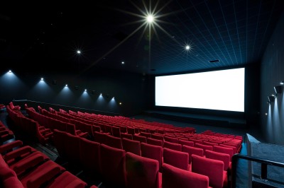 Salle de cinéma vide avec des rangées de sièges rouges et un projecteur allumé au fond.