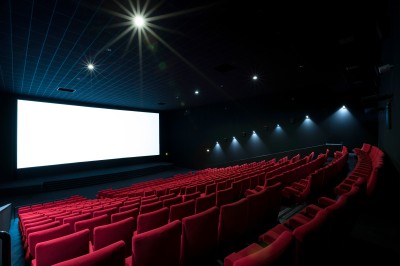 Salle de cinéma vide avec des rangées de sièges rouges et un projecteur allumé au fond.