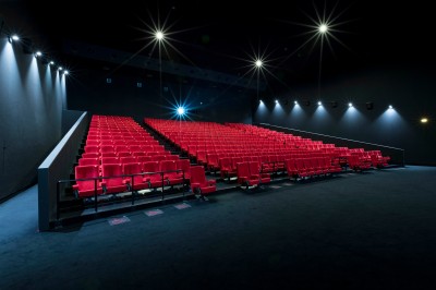 Salle de cinéma vide avec des rangées de sièges rouges et un projecteur allumé au fond.