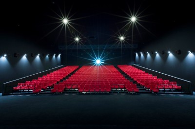 Salle de cinéma vide avec des rangées de sièges rouges et un projecteur allumé au fond.