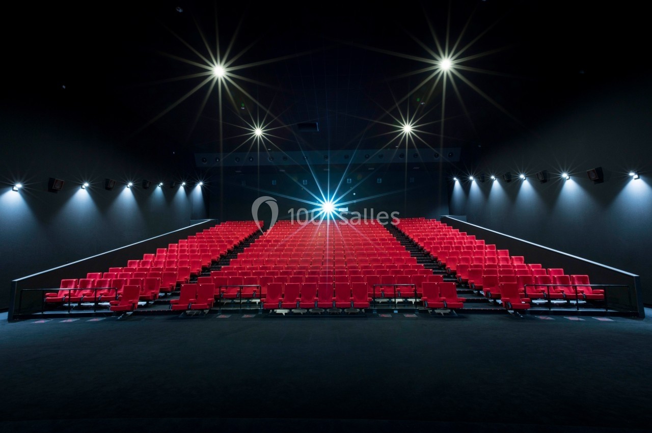 Salle de cinéma vide avec des rangées de sièges rouges et un projecteur allumé au fond.
