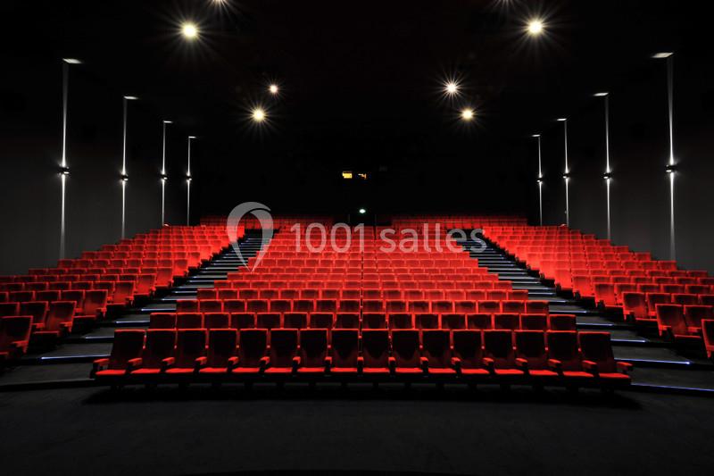 Salle de cinéma vide avec des rangées de sièges rouges et un éclairage tamisé.