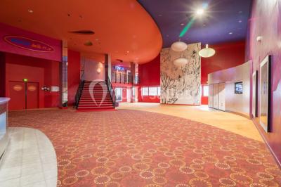 Salle de cinéma vide avec des rangées de sièges rouges, éclairage tamisé et écran en fond.