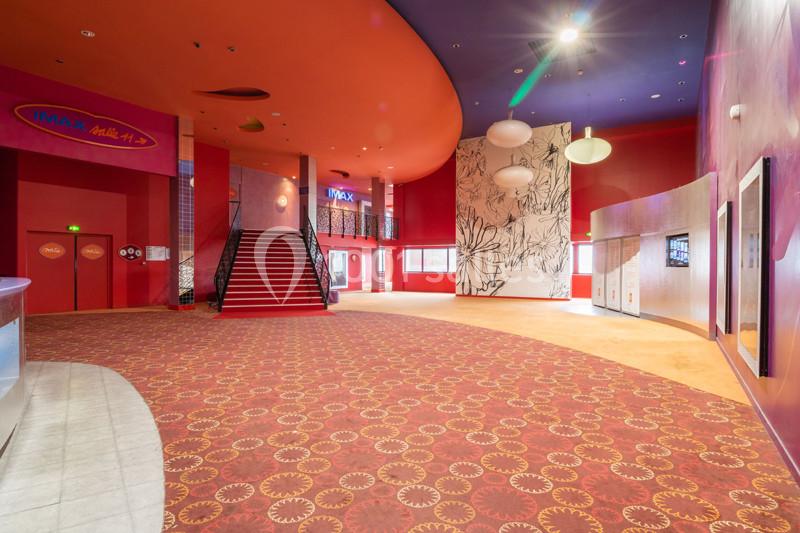 Hall spacieux d'un cinéma avec moquette rouge, escalier central, murs colorés et décorations modernes.