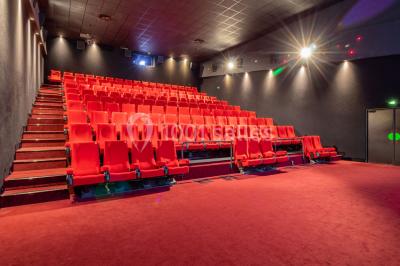 Salle de cinéma vide avec des rangées de sièges rouges, éclairage tamisé et écran en fond.