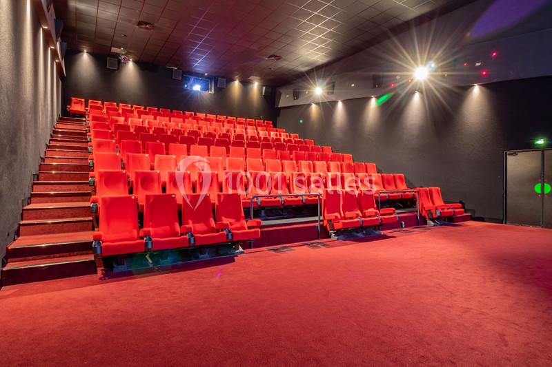 Salle de cinéma vide avec des rangées de sièges rouges et un éclairage tamisé.