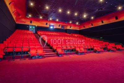 Salle de cinéma vide avec des rangées de sièges rouges, éclairage tamisé et écran en fond.