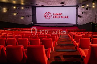 Salle de cinéma vide avec des rangées de sièges rouges, éclairage tamisé et écran en fond.