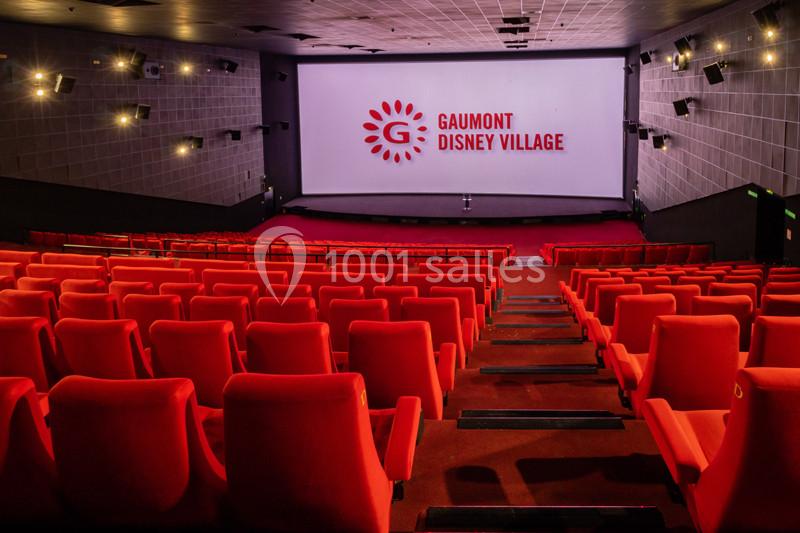 Salle de cinéma vide avec des rangées de sièges rouges et un écran affichant le logo ’Gaumont Disney Village’.