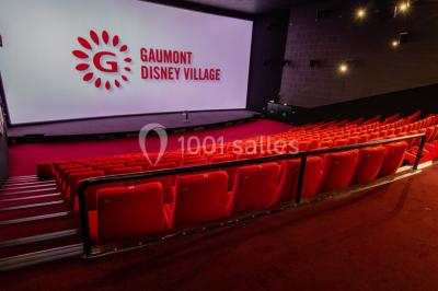 Salle de cinéma vide avec des rangées de sièges rouges, éclairage tamisé et écran en fond.