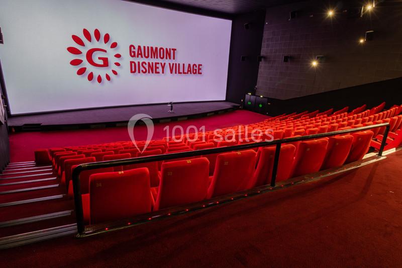 Salle de cinéma vide avec des rangées de sièges rouges et un grand écran affichant ’Gaumont Disney Village’.