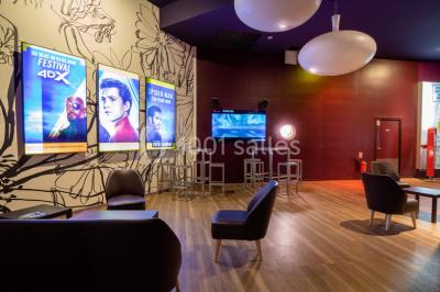 Salle de cinéma vide avec des rangées de sièges rouges, éclairage tamisé et écran en fond.