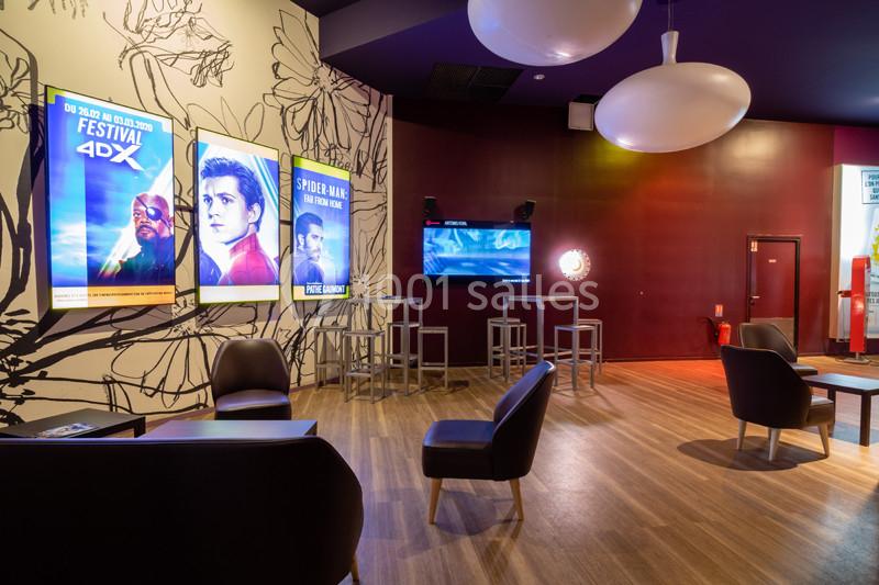 Espace lounge d'un cinéma avec affiches de films, chaises, tables et éclairage tamisé.