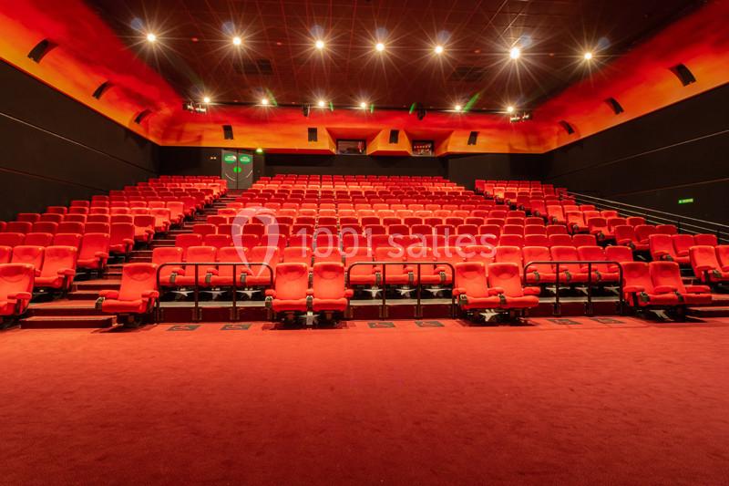 Salle de cinéma vide avec rangées de sièges rouges, éclairage tamisé et écran hors champ.