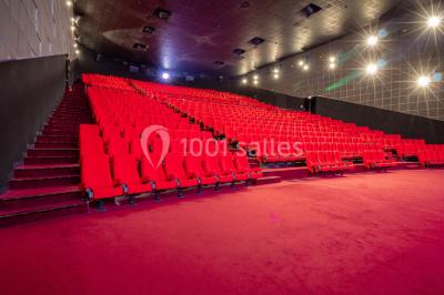 Salle de cinéma vide avec des rangées de sièges rouges, éclairage tamisé et écran en fond.