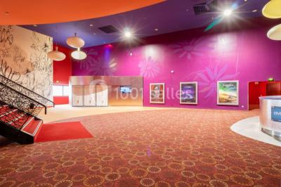 Salle de cinéma vide avec des rangées de sièges rouges, éclairage tamisé et écran en fond.