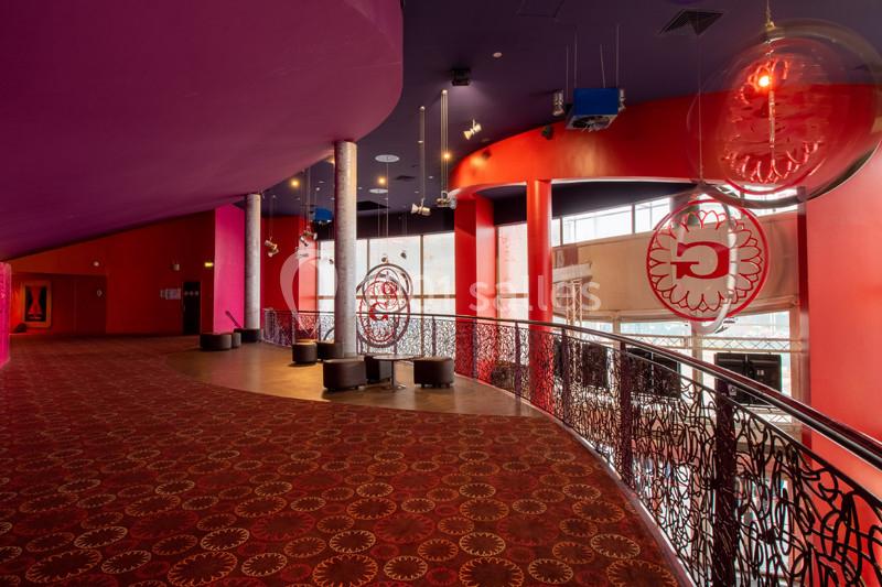 Intérieur d'un espace public coloré avec moquette rouge, balustrade décorative et grandes baies vitrées.