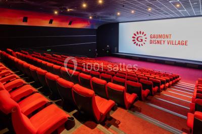 Salle de cinéma vide avec des rangées de sièges rouges, éclairage tamisé et écran en fond.
