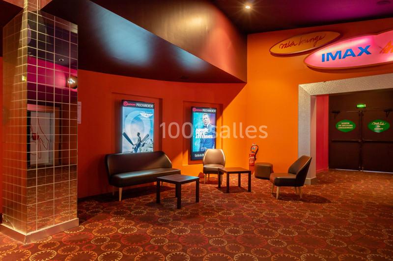 Espace d'attente d'un cinéma avec fauteuils, affiches de films et portes menant à des salles de projection.