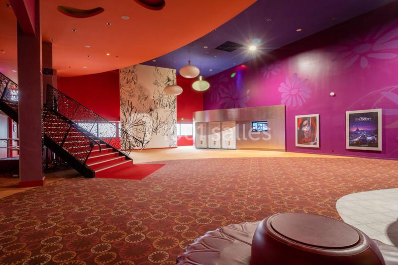 Hall de cinéma coloré avec moquette à motifs, affiches de films, escalier noir et murs décorés de fleurs.