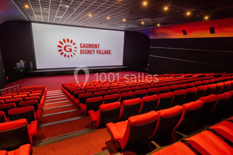Salle de cinéma vide avec des sièges rouges, un écran géant et le logo ’Gaumont Disney Village’ affiché.