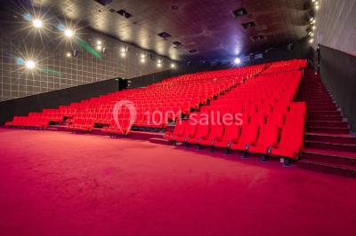 Salle de cinéma vide avec des rangées de sièges rouges, éclairage tamisé et écran en fond.