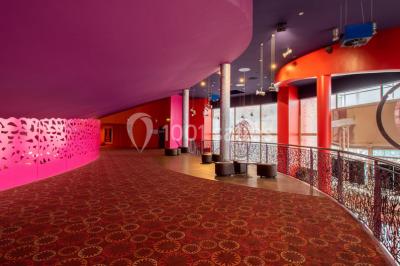 Salle de cinéma vide avec des rangées de sièges rouges, éclairage tamisé et écran en fond.
