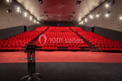 Salle de cinéma vide avec des rangées de sièges rouges, éclairage tamisé et écran en fond.