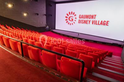 Salle de cinéma vide avec des rangées de sièges rouges, éclairage tamisé et écran en fond.