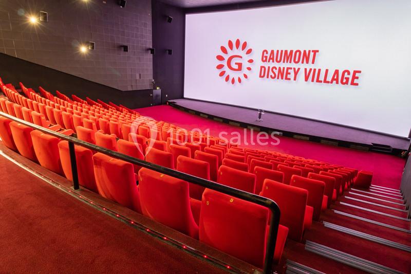 Salle de cinéma avec rangées de sièges rouges et grand écran affichant le logo ’Gaumont Disney Village’.