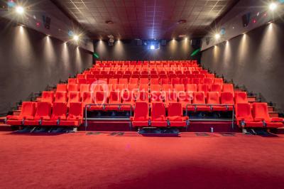 Salle de cinéma vide avec des rangées de sièges rouges, éclairage tamisé et écran en fond.