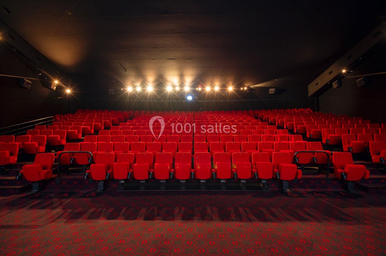 Salle de cinéma vide avec des rangées de sièges rouges et un éclairage tamisé au plafond.