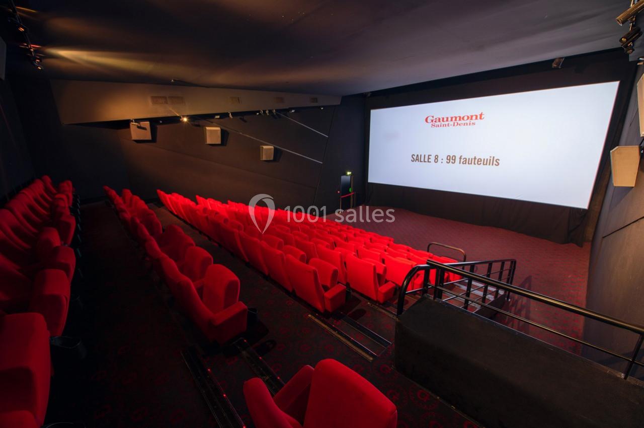 Salle de cinéma vide avec des fauteuils rouges, écran blanc affichant ’Gaumont’ et la capacité de 99 fauteuils.