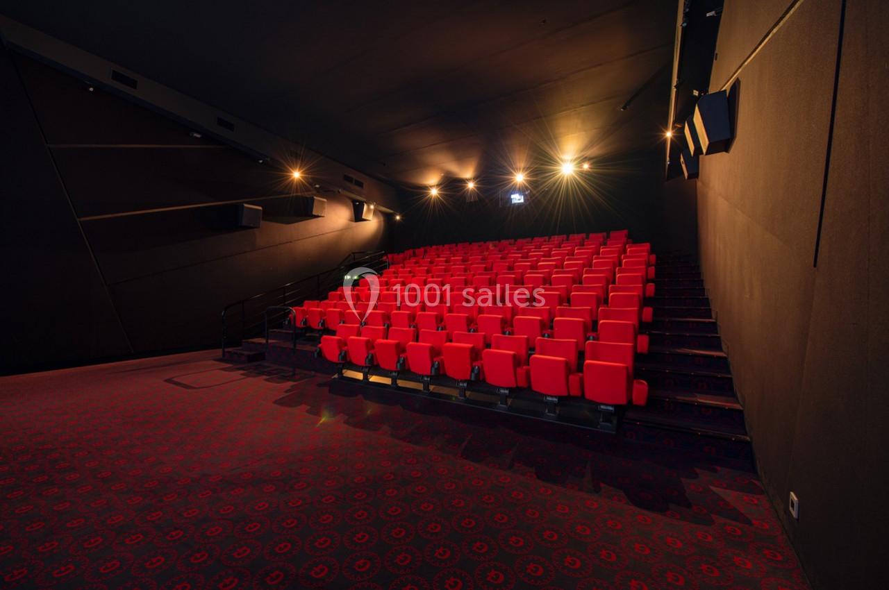 Salle de cinéma vide avec des rangées de sièges rouges et un éclairage tamisé.